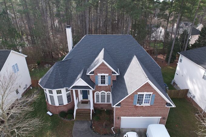 default Aerial drone view of a brick two-story home with a new dark gray shingle roof surrounded by pine trees in Raleigh, NC