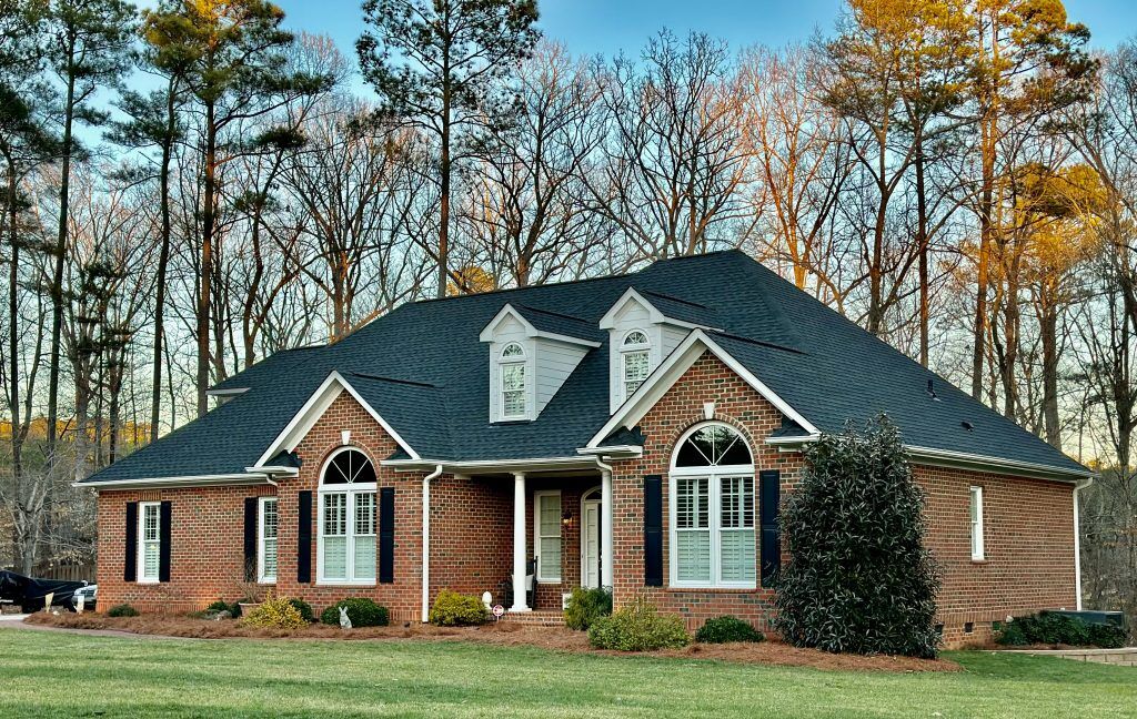 Large brick home with a covered front porch and newly installed dark shingle roof in Myrtle Beach, SC