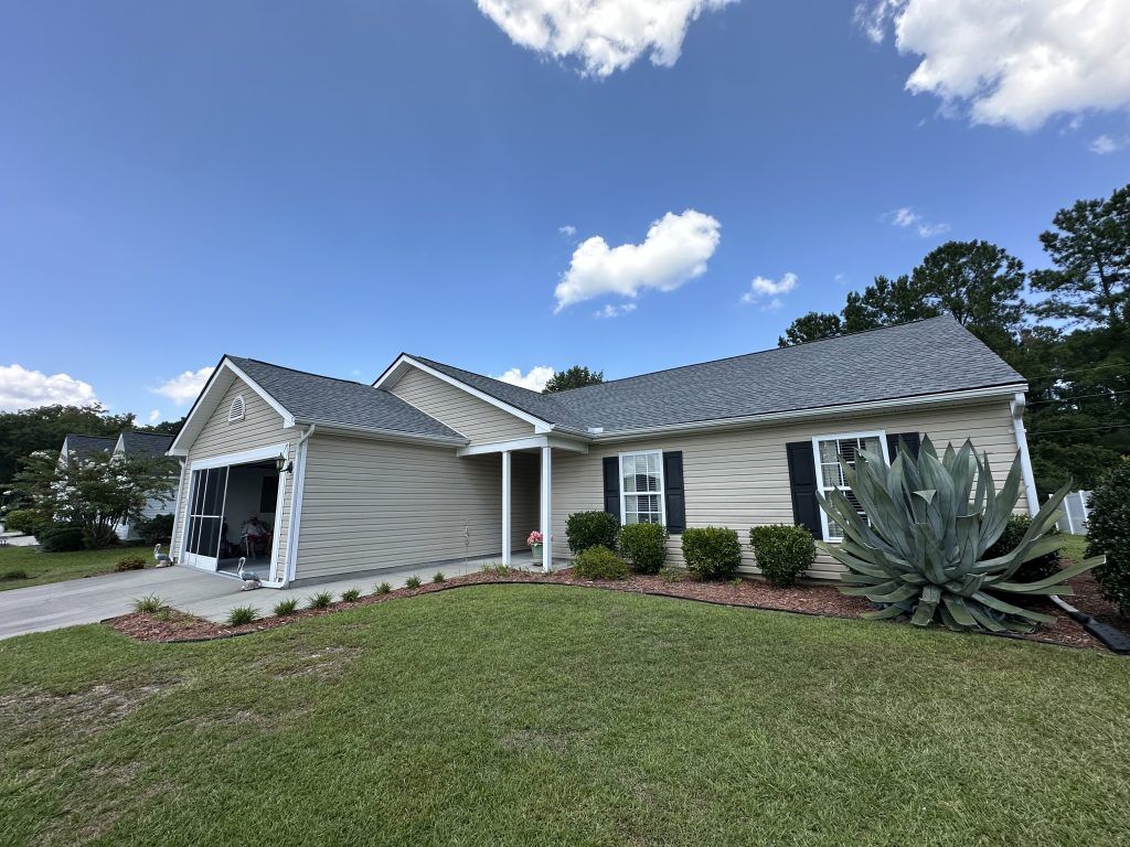 Tan single-story home with new dark gray shingle roof under a partly cloudy sky in Myrtle Beach, SC