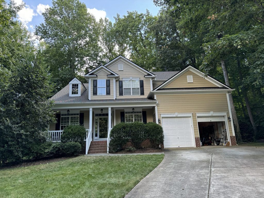 item_9cfd9ed4-c6e6-41df-b988-6a3d4728e5bc Two-story brick home with a newly installed dark shingle roof in a wooded neighborhood in Raleigh, NC